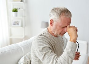 Älterer Mann sitzt auf einem Sofa und hält sich nachdenklich die Stirn | © PflegeBetreuer | unabhängige Pflegeberatung