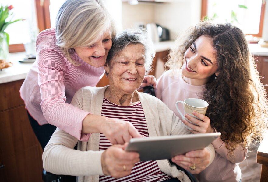 Seniorin sitzt mit zwei Angehörigen am Tablet und nutzt einen Online-Pflegekurs zur Unterstützung im Pflegealltag. | © PflegeBetreuer | unabhängige Pflegeberatung