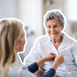 Betreuungskraft hilft einer älteren Frau beim Zuknöpfen ihrer Bluse | © PflegeBetreuer | unabhängige Pflegeberatung