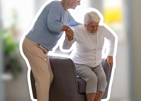 Pflegende Angehörige unterstützt ältere Frau beim Aufstehen aus dem Sessel im Wohnzimmer – symbolisches Bild zur Rente für pflegende Angehörige | © PflegeBetreuer | unabhängige Pflegeberatung